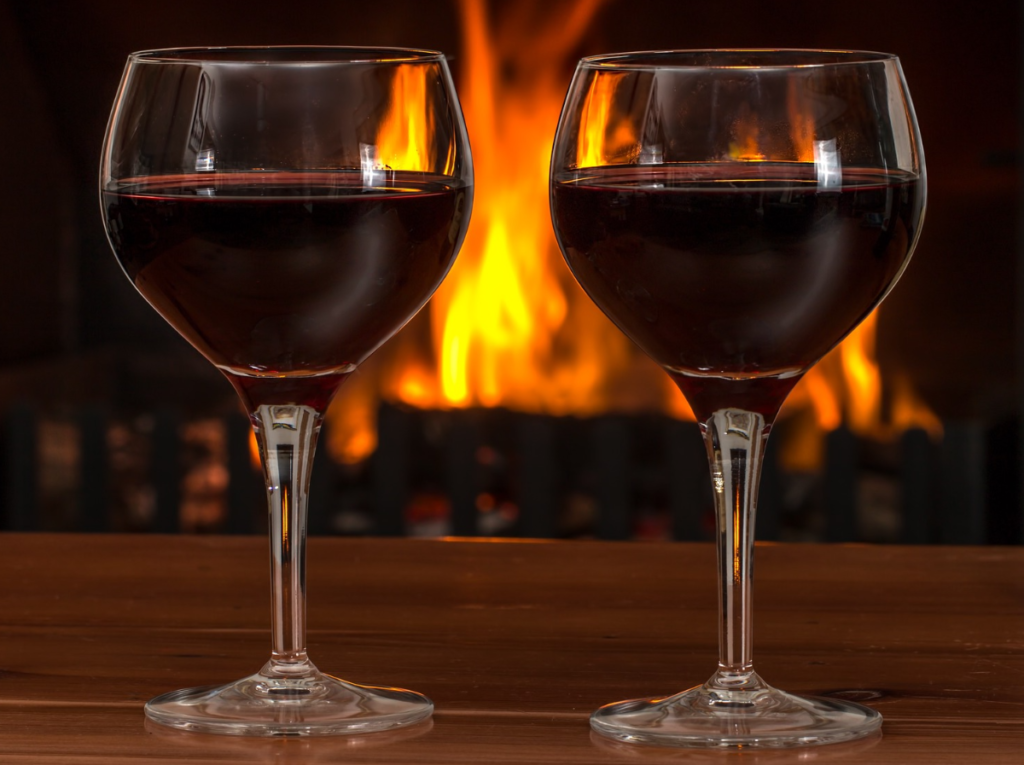 deux verres de vins rouges devant un feu de cheminée